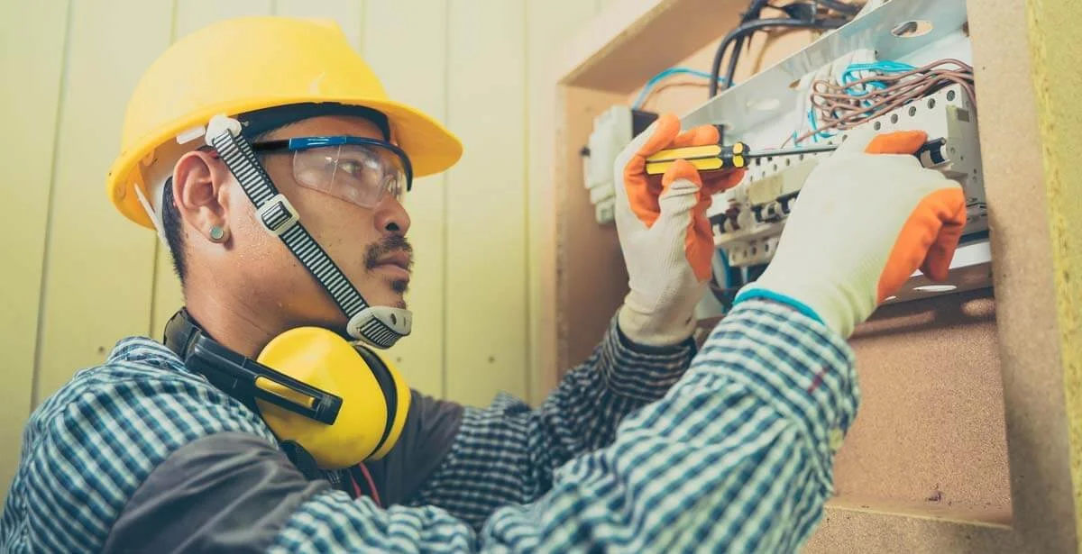 Electrician in safety gear working on electrical panel