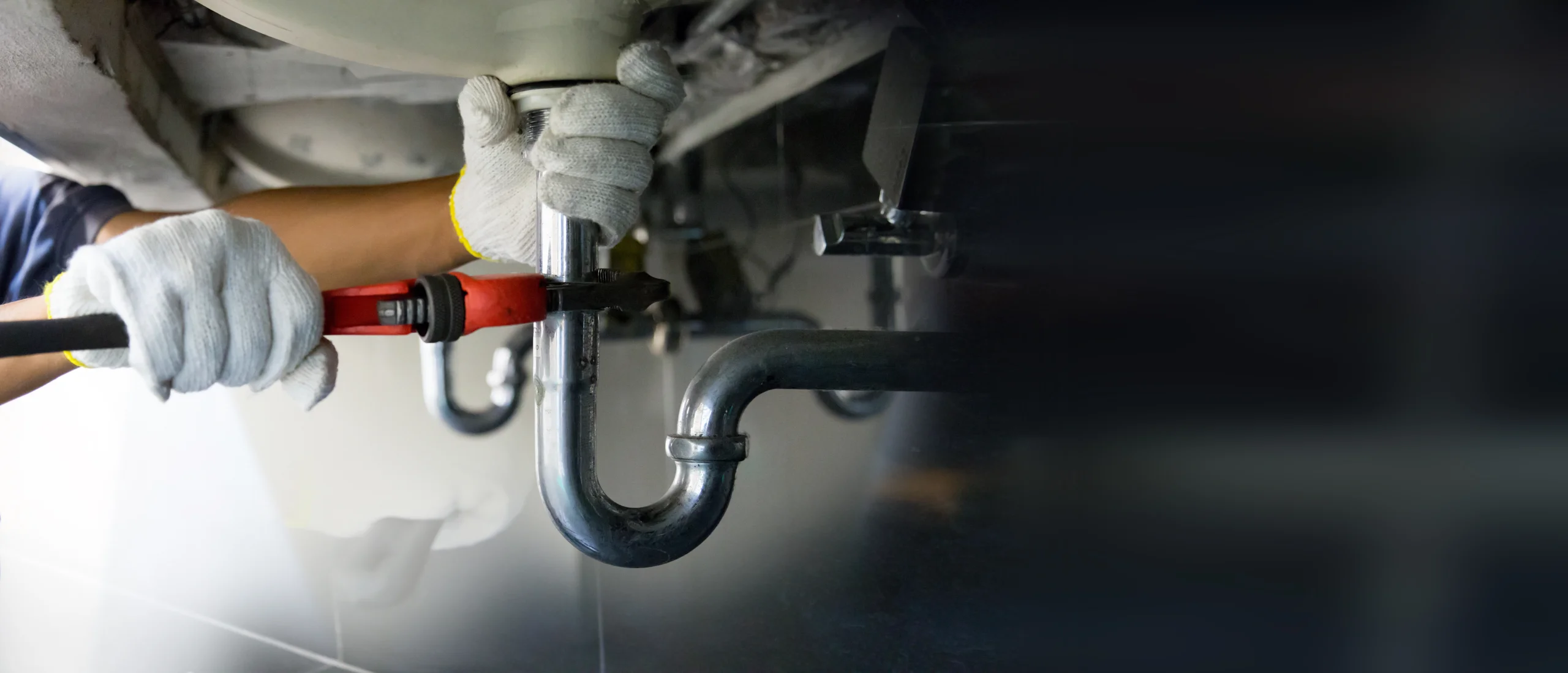 Plumbing technician using a wrench to fix pipe under sink