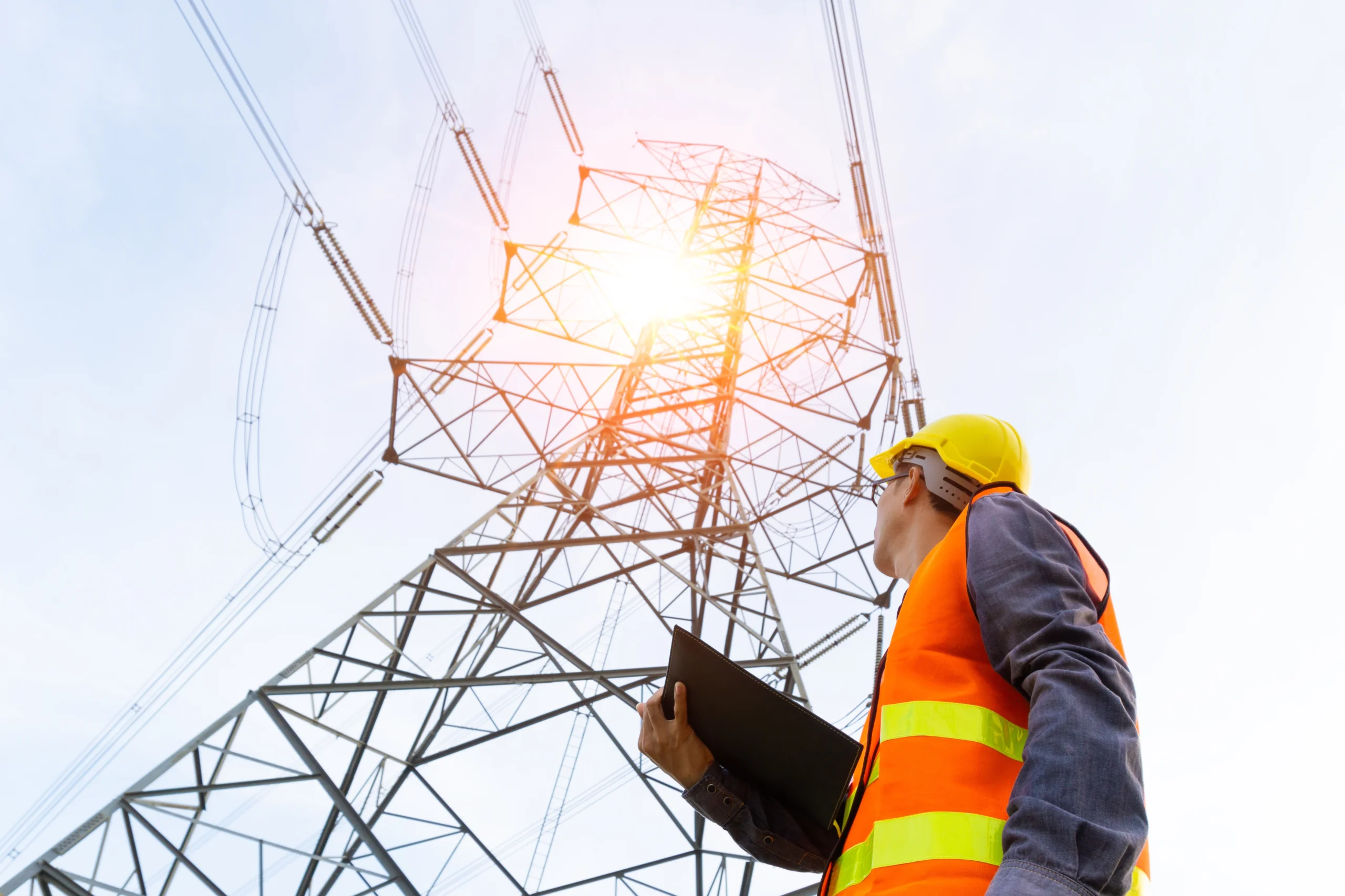 Electrical technician looking up at electrical power lines